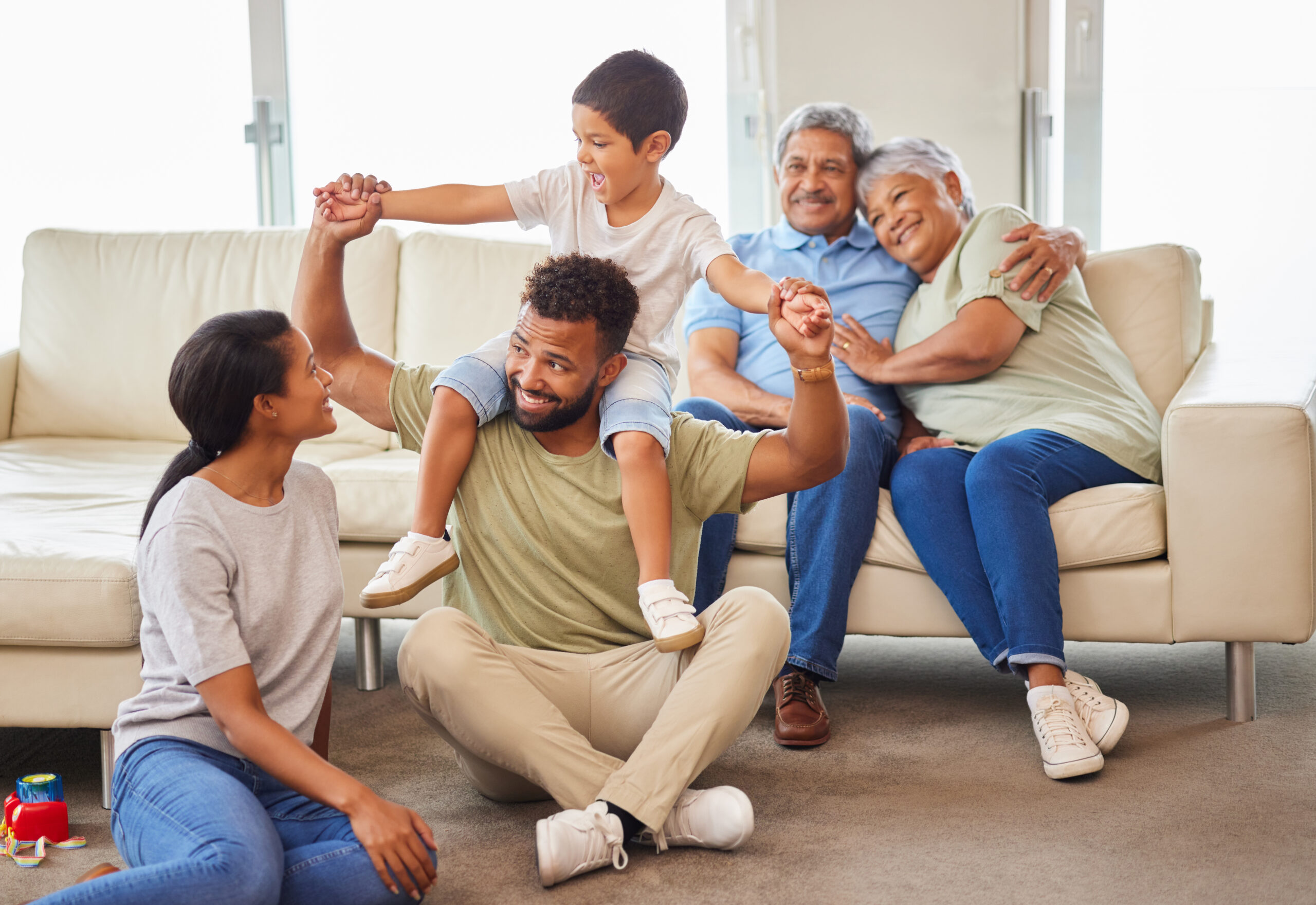 A mixed race family bonding together while parents playing with the kids while the grandparents relax on the couch at home